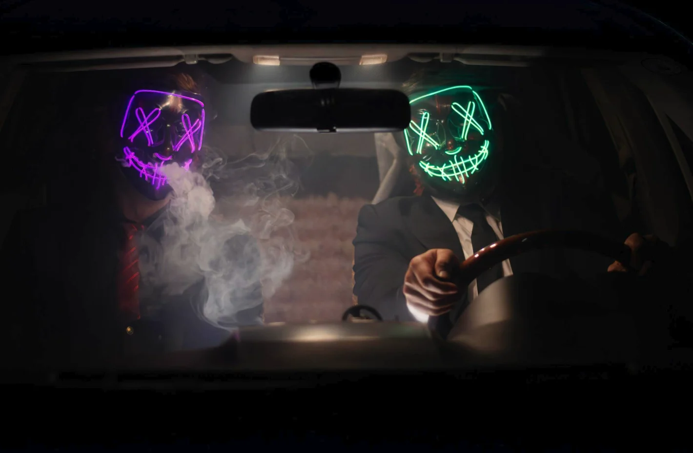 Two people with neon masks in smoky car - suggesting criminality