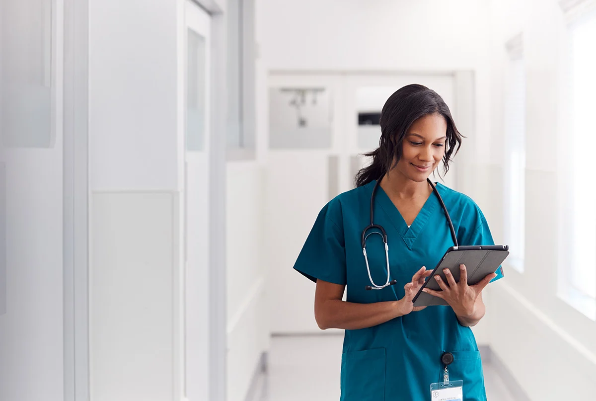 A nurse walking down a hall with a tablet in hand.