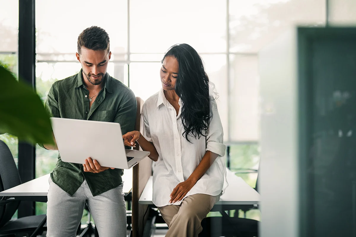 two people sitting on a desk looking at a laptop.