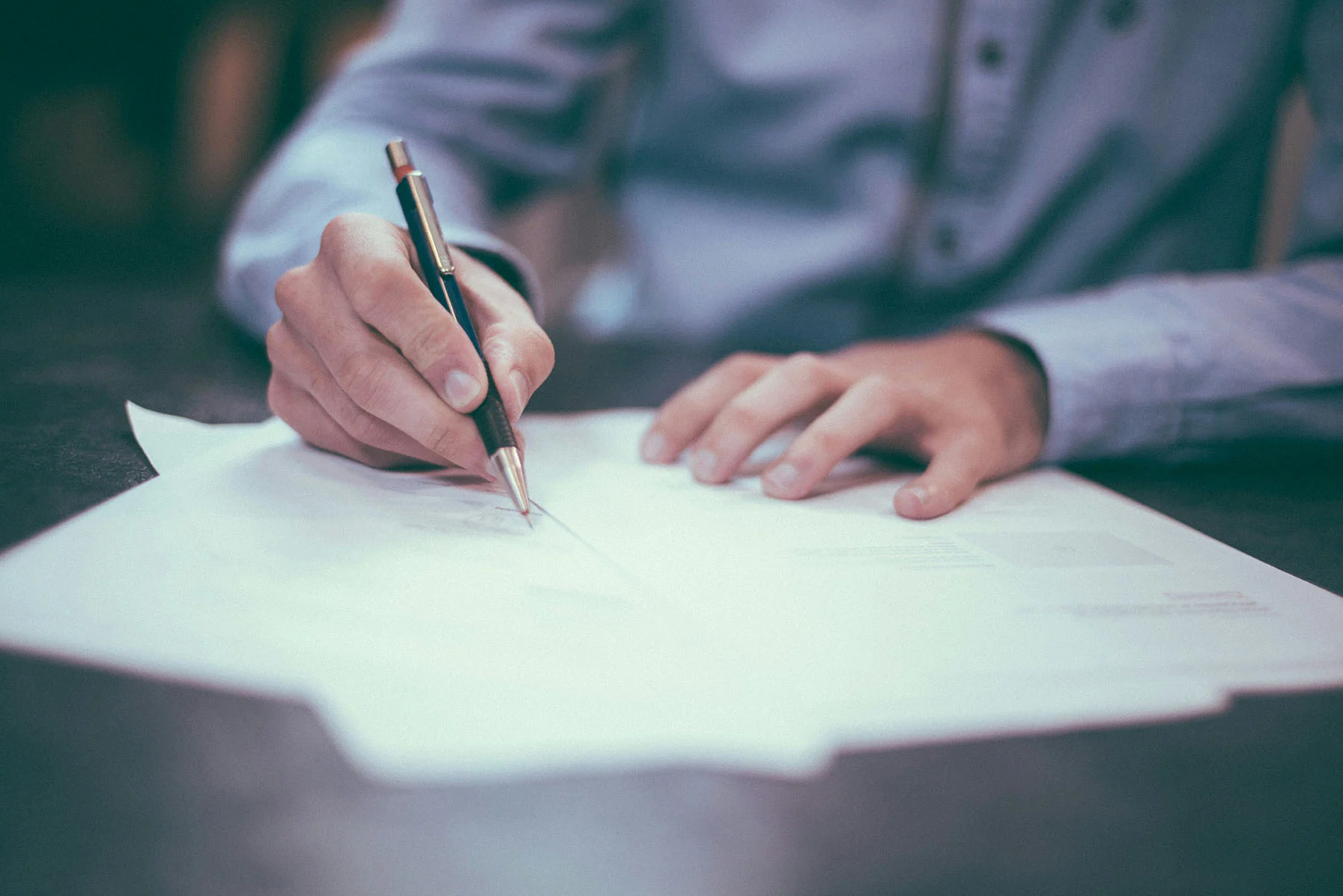 close up of man writing on a piece of paper with a pen.